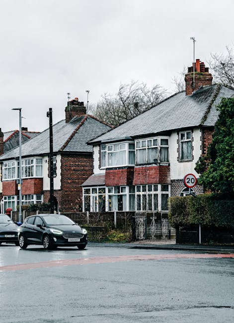 A white moving van with a closed cargo area is positioned on a city street, right outside a multi-storey, historic-style building with ornate architectural details and numerous arched windows. The van